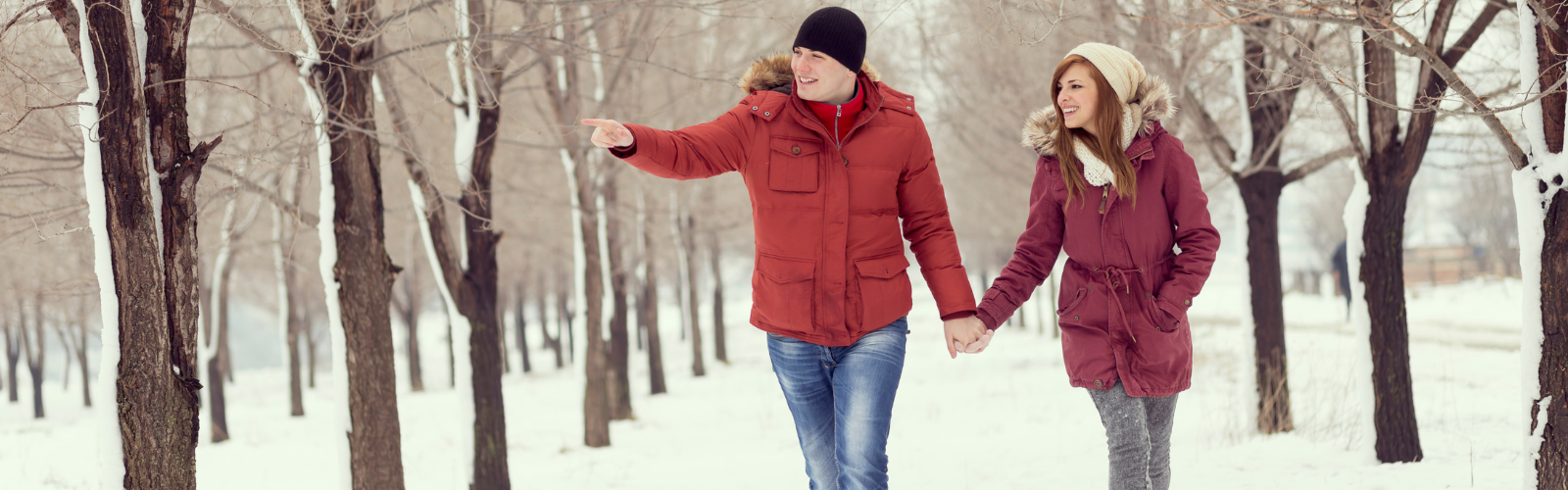 A couple on vacation holds hands while walking through a park covered in snow.