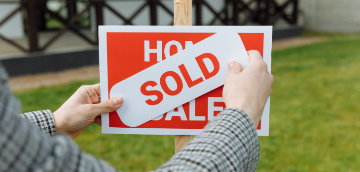 A "sold" sticker is placed on a "home for sale" sign.