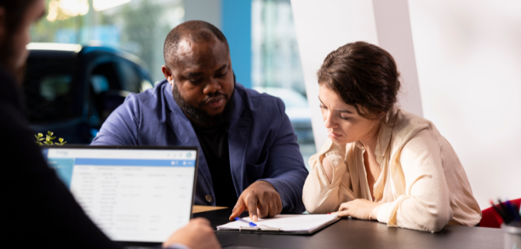 A couple sits in the dealership, intently reading every detail of their auto loan contract. They're not sure if this is the best deal they could have gotten.