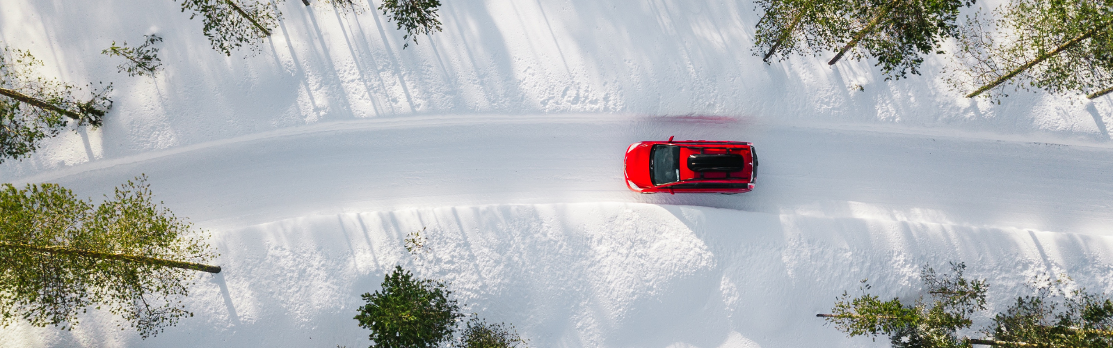An overhead shot of a bright red car driving along a winding snow-covered road.