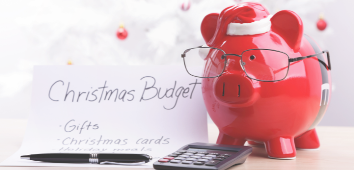 A full piggy bank with a Santa hat next to a calculator and a Christmas budget