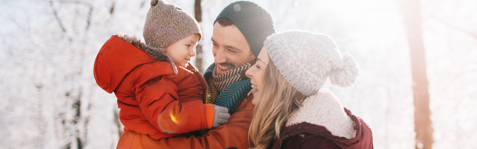A family of three hold each other in a snowy forest with a joyful expression.